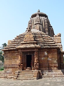 The entrance to a structure with depictions of nagins and guarding deities in the doorjambs, with a tower in the background