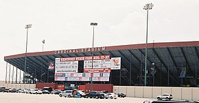 A ballpark's red and gray bleachers viewed from its parking lot