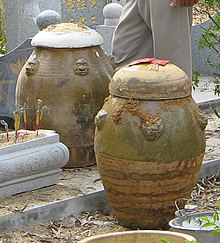 Two large, rounded urns with ochre and faded green decorative elements. They are fitted with rounded lids and come to just above knee height.