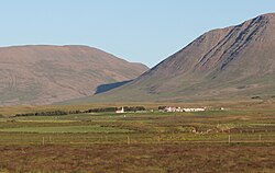 View of the estate and church in Viðvík in a valley with mountains in the background