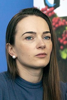Oleksandra Matwijtschuk hat langes dunkelblondes Haar und trägt einen blauen Pullover. Der Hintergrund ist blau und sie trägt weiße Perlenohringe.
