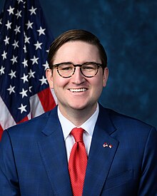 Official House portrait of McDowell smiling in front of the U.S. flag, wearing a dark blue suit with American and North Carolinian flags lapel pin, white shirt, and red tie.