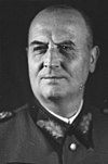 A black-and-white up-and-front photograph of a smiling man wearing a military uniform.