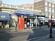 A white-bricked building with a clear, sloped roof and a sign that reads "BAYSWATER STATION" in white letters on a blue background