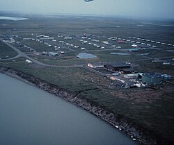 An aerial view of Nuiqsut, showing lines of structures evenly spaced and laid out in a rectangle along the shore of a river