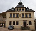 Wohnhaus in offener Bebauung, zeitweise Hotel mit Gaststätte, heute katholisches Pfarramt und Kirche, mit Torbogen (zum Nachbarhaus Nr. 25)