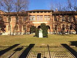 A large building set on an expansive lawn, surrounded by trees and clear skies.