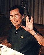 An Asian man wearing a black shirt gives a Vulcan salute.