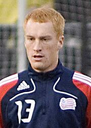 A soccer player is wearing a New England Revolution warm-up jacket.