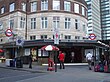 A brown-bricked building with a rectangular, dark blue sign reading "WARREN STREET STATION" in white letters and people in front