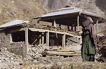 Eine Mutter mit ihrem Kind steht vor ihrem zerstörten Haus in Nardjan