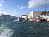 Foto mit einigen Hafengebäuden auf der rechten Seite, einige Boote im Wasser davon und zwei Inseln im Hintergrund