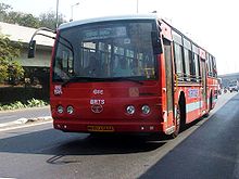 A red bus on a road. Blue letters are seen on its side