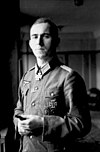 A man holding a cigar in his left hand, wearing a military uniform and an Iron Cross displayed at the front of his uniform collar.