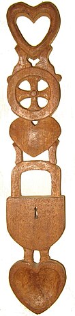 Welsh carved wooden lovespoon with hearts, lock and wheel. There are five design elements, three hearts which also form the bowl and the ring of the spoon. Between these are a wheel and a padlock.