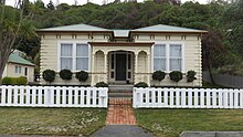 An Edwardian-style house with a white picket fence and a forested background