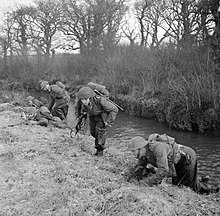 Soldiers from the division training, take cover along a river bank.