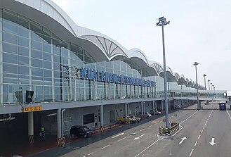 A curvy roof airport exterior with glass windows and the apron superimposed at the bottom.