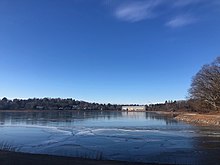 Ice on surface of the reservoir in January. View across of trees and stadium.