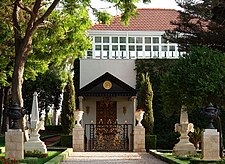 Stone pathway surrounded by gardens leading to a building with golden gates.