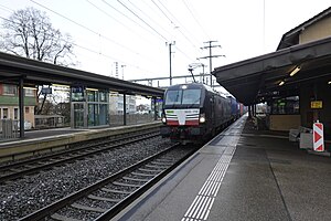 Freight train passing by the station next to a three-story building with gabled roof