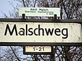 Straßenschild mit Namenserläuterung und Hausnummernhinweis