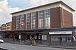 A brown-bricked building with a flat-slabbed roof and six columns of windows on the front face standing below a blue sky with white clouds