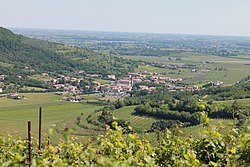 A hilly landscape with a small town with white buildings, red roofs, and a belltower.