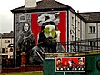 Gable-end mural, vandalised with green paint,[note 22] showing Raymond McCartney and a female hunger striker from 1980