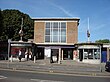 A brown-bricked building with a blue sign reading "EASTCOTE STATION" in white letters and people walking in front all under a blue sky with white clouds