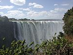 A view of dozens of waterfalls side-by-side crashing into the water below. A rainbow forms at the right.