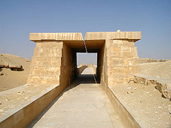 A paved way of white limestone covered with a roof made of massive stone blocks resting on equally massive walls.