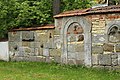 Steinelemente einer alten gotischen Kirche, eingemauert in eine Friedhofsmauer