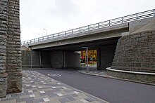 Curving limestone towers support a bridge crossing over a modern road.