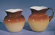 small cream pitcher with white glass on inside and dark orange on outside top with cream colored glass on bottom half