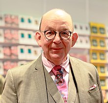 Denis Scheck im Anzug mit Krawatte gekleidet vor einer Bücherwand auf der Frankfurter Buchmesse 2022