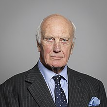 Head and shoulders of a balding grey-haired man in a pinstripe suit