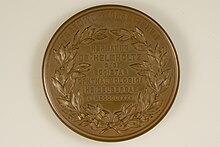 Die Rückseite der bronzenen Graefe-Medaille zeigt sieben zentrierten geprägte Zeilen jeweils in Versalschrift: „HERMANNO“, „DE • HELMHOLTZ“, „D • D“, „SOCIETES“, „OPTHALMOLOGICA“, „HEIDELBERGAE“, „A • MDCCCLXXXVI“. Der Schriftblock wird durch ein Lorbeerkranz gerahmt. Oben am Rand sind die beiden Worte „PRAEMIVM“ „GRAEFIANVM“ wiederum Versalschrift eingeprägt