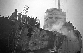 large holes in side of the ship. A ladder leads to the dock. There is also evidence of a fire.