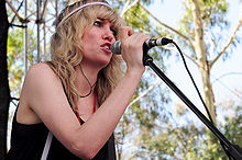 A woman wearing a black singlet and pink hairband, singing into a microphone