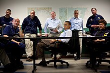 Photo of Obama listening to a briefing, surrounded by senior staffers
