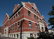 A small brick and stone building, seen from the corner view, in front of clear blue sky