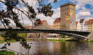 Die Dreiradenmühle an der Lausitzer Neiße, mit dem Mosaikgesicht (WAZE) vorne die Altstadtbrücke, im Hintergrund der Zgorzelecer Postplatz