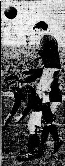 A black and white image of a footballer jumping to head a ball.