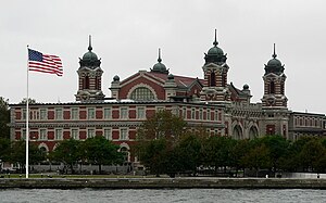 A large three-story brick-red building whose windows are outlined in white. It has four towers, each with a cupola and spikes at the top.