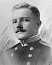 Head and shoulders of a white man with a neatly trimmed mustache wearing a military jacket with shoulder boards and two columns of buttons down the chest.