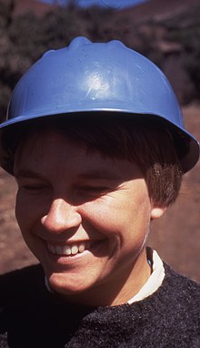 Physicist Ann Merchant Boesgaard, around age 30, wears a blue hard hat and smiles, looking off camera to the left.