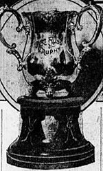 Black and white photo of a silver bowl trophy with two large handles, mounted on a black plinth.