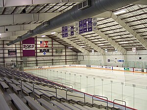 The inside of an ice hockey arena. An empty ice hockey surface is at the base of rows of spectator benches.