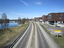 Foto einer Straße, rechts davon Häuser, links ein breiterer Fluss